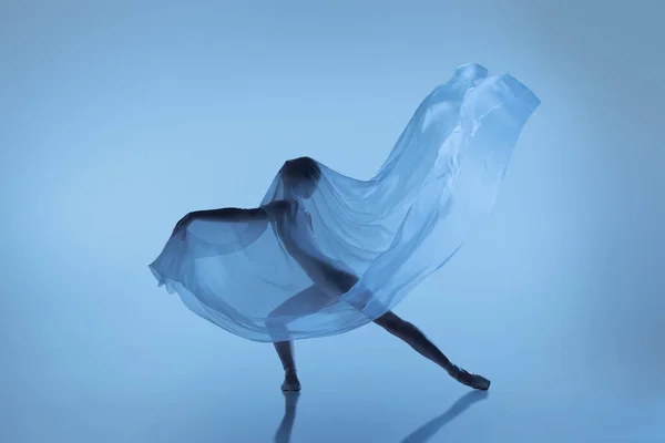 Ritratto di donna flessibile, ballerina graziosa che balla con tessuto, panno isolato su sfondo blu da studio. Grazia, arte, concetto di bellezza. Senza peso, tenerezza. — Foto Stock