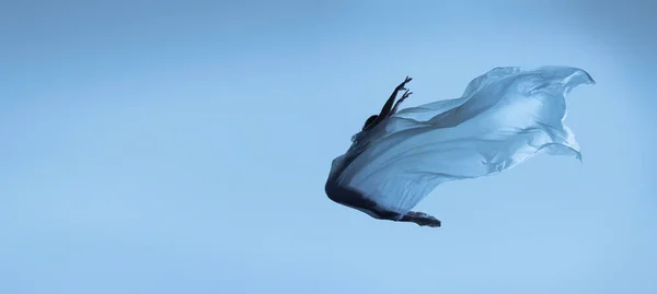 Potret wanita yang fleksibel, balerina yang anggun menari dengan kain, kain terisolasi di latar belakang studio biru. Grace, seni, konsep kecantikan. Berat badan, kelembutan. — Stok Foto