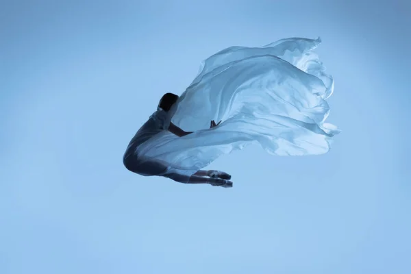 Esnek kadın portresi, kumaşla dans eden zarif balerin mavi stüdyo arka planında izole edilmiş kumaş. Zarafet, sanat, güzellik konsepti. Ağırlıksız, şefkatli.. — Stok fotoğraf