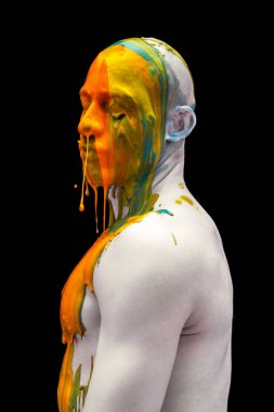 Gözleri kapalı duran genç adamın yaratıcı portresi. Renkli boyalar, boyalar kafasından, omuzlarından ve vücudundan aşağı akıyor..