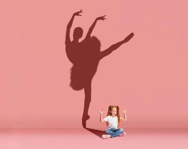A kis vörös hajú lány arról álmodik, hogy balett táncos lesz, rózsaszín háttérrel elszigetelve. Sport, karrier és álmok koncepció. Kollázs — Stock Fotó
