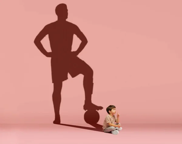 Mały chłopiec marzy o zostaniu futbolistą odizolowanym na różowym tle. Koncepcja dzieciństwa i marzeń. Kolaż. — Zdjęcie stockowe