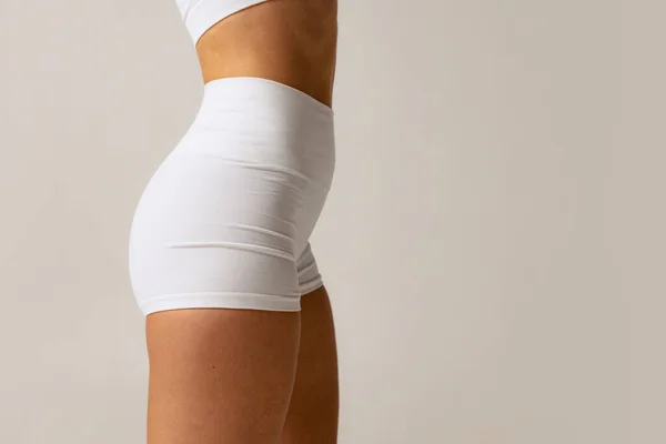 Citra studio yang dipotong tipis, tubuh perempuan sportif dengan pakaian putih nyaman terisolasi di atas latar belakang abu-abu. Tampilan samping — Stok Foto