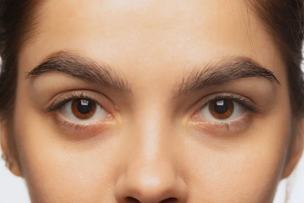 Imagem de close-up recortada de belos olhos castanhos femininos olhando para a câmera isolada sobre fundo estúdio branco — Fotografia de Stock