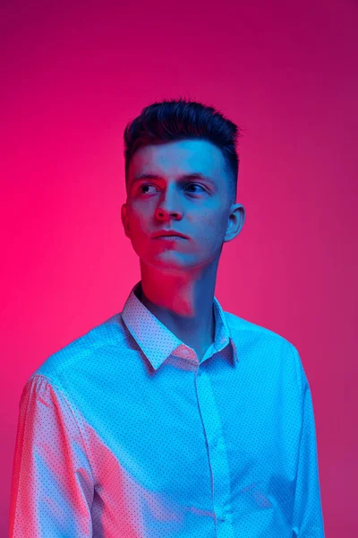 Portrait mi-long de jeune homme beau en chemise blanche posant isolé sur fond studio couleur magenta en néon bleu — Photo