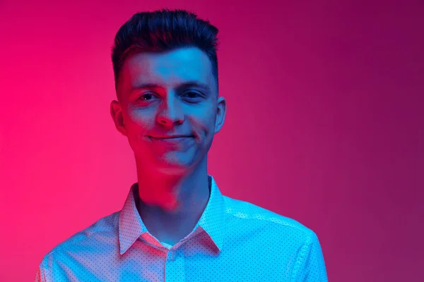 Jovem homem feliz em camisa branca sorrindo isolado sobre fundo estúdio cor magenta em luz de néon azul. Conceito de emoções positivas — Fotografia de Stock
