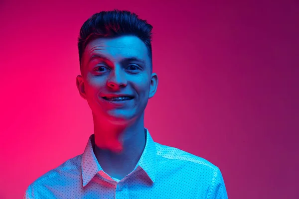 Jovem homem feliz em camisa branca sorrindo isolado sobre fundo estúdio cor magenta em luz de néon azul. Conceito de emoções positivas — Fotografia de Stock
