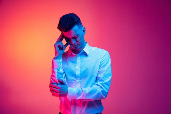 Retrato de meio comprimento de homem bonito jovem na camisa branca tem uma terrível dor de cabeça isolada sobre cor magenta fundo sttudio em luz de néon azul — Fotografia de Stock