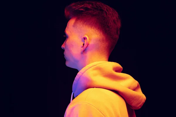 Visão de perfil do jovem usando capuz isolado sobre fundo escuro estúdio em luz de néon. Conceito de emoções, moda — Fotografia de Stock