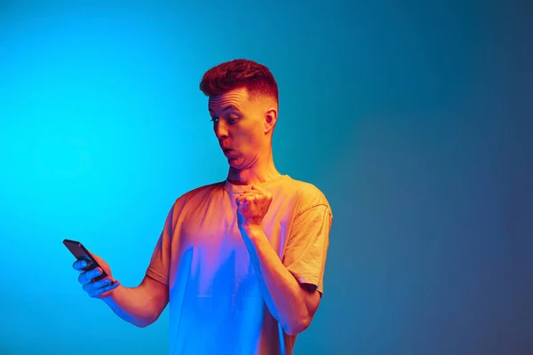 Estúdio tiro de jovem homem emocional, estudante usando smarphone isolado sobre fundo estúdio azul. Ação, esporte, moda — Fotografia de Stock