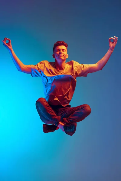 Porträt eines jungen, ruhigen Mannes, Studenten, die in Lotusposition in der Luft sitzen, isoliert über blauem Studiohintergrund. Action, Sport, Mode — Stockfoto