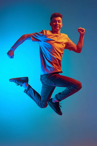 Retrato dinámico del joven emocionado, estudiante saltando alegremente en la emoción aislado sobre fondo azul del estudio. Acción, deporte, moda —  Fotos de Stock