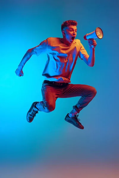 Dynamiskt porträtt av ung upphetsad man, student glatt hoppa i spänning isolerad över blå studio bakgrund. Åtgärd, idrott, mode — Stockfoto