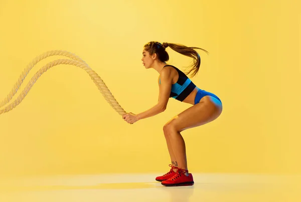 Retrato de una joven deportista entrenando con cuerdas deportivas aisladas sobre fondo amarillo del estudio. Deporte, acción, fitness, juventud y concepto de salud. — Foto de Stock