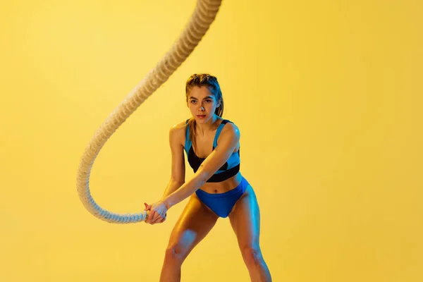 Retrato de treinamento jovem menina esportiva com cordas esportivas isoladas no fundo do estúdio amarelo. Esporte, ação, fitness, juventude e conceito de saúde. — Fotografia de Stock