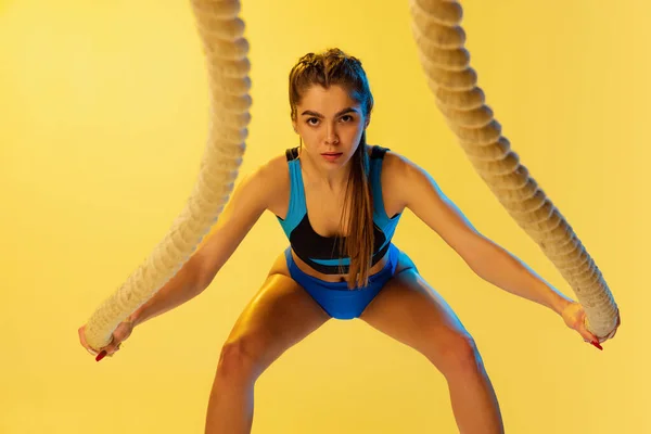 Retrato de treinamento jovem menina esportiva com cordas esportivas isoladas no fundo do estúdio amarelo. Esporte, ação, fitness, juventude e conceito de saúde. — Fotografia de Stock