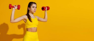 Stüdyoda spor malzemeleriyle spor yapan zayıf bir kızın parlak sarı stüdyo arka planında gölgeli görüntüsü. Güzellik, spor, aksiyon, fitness, gençlik konsepti.