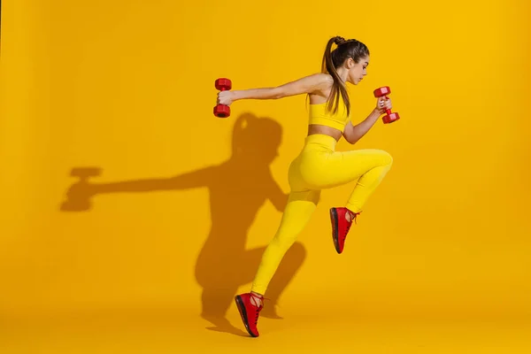 Studio záběr sportovní štíhlé dívka cvičení se sportovním vybavením izolované na jasně žlutém pozadí studia se stínem. Krása, sport, akce, fitness, koncepce mládeže. — Stock fotografie