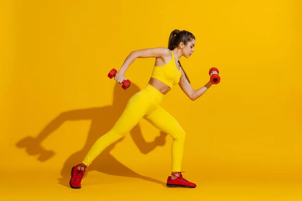 Studyjne ujęcie sportowego treningu szczupłej dziewczyny ze sprzętem sportowym odizolowanym na jasnożółtym tle studio z cieniem. Piękno, sport, działanie, sprawność, koncepcja młodzieży. — Zdjęcie stockowe