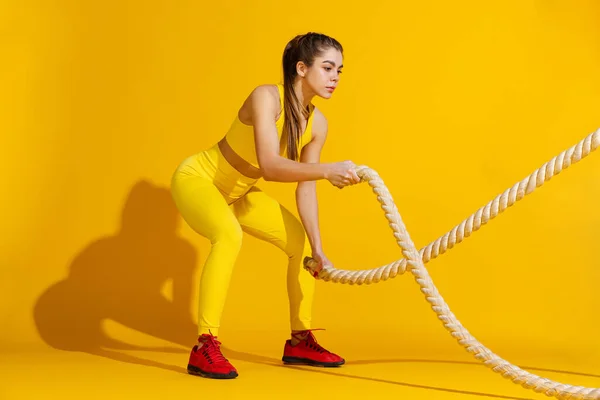 Студійний знімок спортивної стрункої дівчини тренування зі спортивним обладнанням ізольовані на яскраво-жовтому студійному фоні з тіні. Краса, спорт, дія, фітнес, молодіжна концепція . — стокове фото