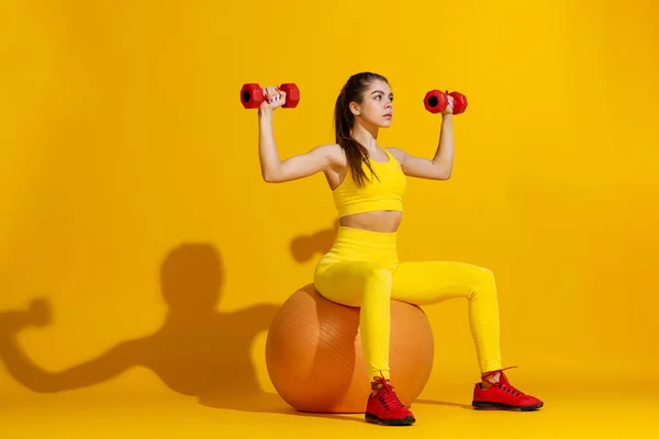 Estudio de entrenamiento deportivo chica delgada con equipos deportivos aislados sobre fondo de estudio de color amarillo brillante con sombra. Belleza, deporte, acción, fitness, concepto de juventud. —  Fotos de Stock