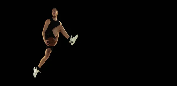 플라이어. 검은 색 제복을 입은 농구 선수, 어두운 배경에서 격리 된 소년의 다이나믹 초상화. 업적, 스포츠 경력, 운동 개념. — 스톡 사진