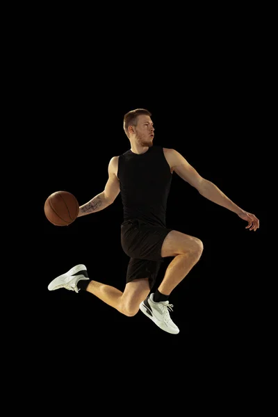 Dynamický portrét mladého muže, basketbalista v černých uniformách, trénink izolovaný na tmavém pozadí. Úspěchy, sportovní kariéra, koncepce pohybu. — Stock fotografie