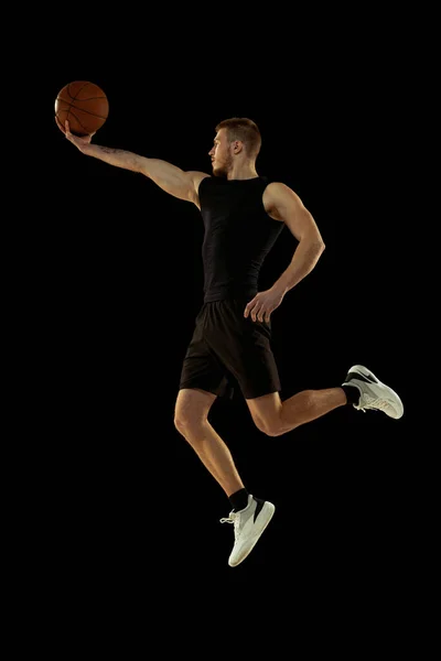 Dynamický portrét mladého muže, basketbalista v černých uniformách, trénink izolovaný na tmavém pozadí. Úspěchy, sportovní kariéra, koncepce pohybu. — Stock fotografie