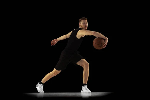 Retrato dinâmico de homem jovem, jogador de basquete em treinamento uniforme preto isolado em fundo escuro. Conquistas, carreira esportiva, conceitos de movimento. — Fotografia de Stock