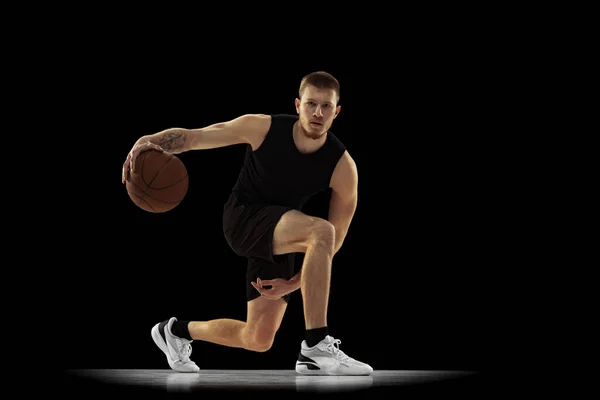 Movimento terrestre. Retrato dinâmico de homem jovem, jogador de basquete em treinamento uniforme preto isolado em fundo escuro. Conquistas, carreira esportiva, conceitos de movimento. — Fotografia de Stock