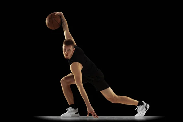 地上へ移動。暗い背景に隔離された黒の均一な訓練の若い男、バスケットボール選手のダイナミックな肖像画。業績、スポーツキャリア、運動概念. — ストック写真