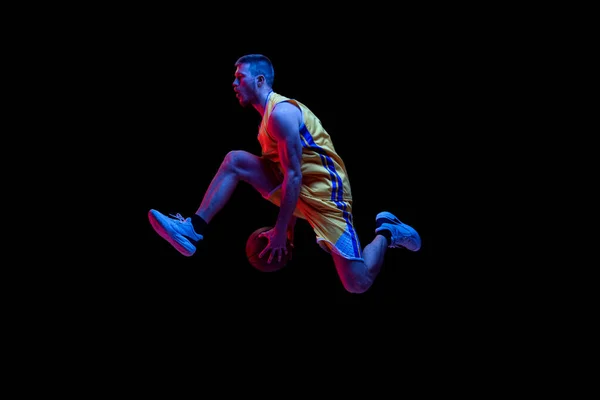 Portret van sportieve man, professionele basketbalspeler die basketbal speelt geïsoleerd op donkere achtergrond in neon licht. Resultaten, sportcarrière, bewegingsconcepten. — Stockfoto