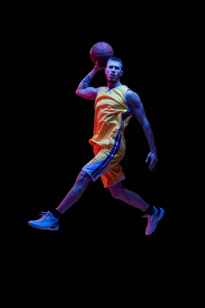 Portret van sportieve man, professionele basketbalspeler die basketbal speelt geïsoleerd op donkere achtergrond in neon licht. Resultaten, sportcarrière, bewegingsconcepten. — Stockfoto