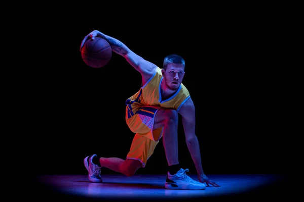Portrait of sportive man, professional basketball player playing basketball isolated on dark background in neon light. Achievements, sport career, motion concepts.