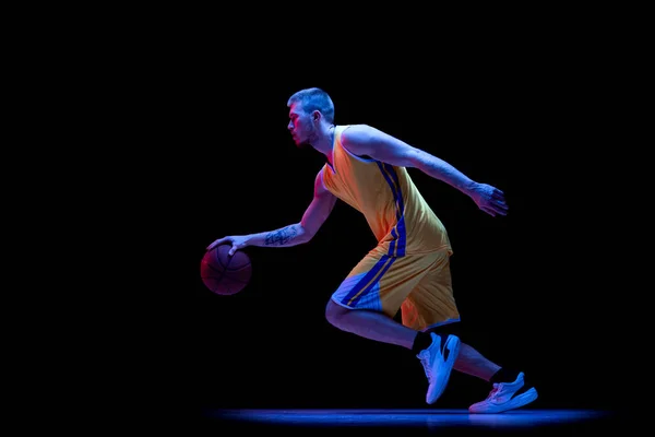 A driblar. Um homem esportivo, jogador de basquete profissional jogando basquete isolado em fundo escuro em luz de néon. Conquistas, carreira esportiva, conceitos de movimento. — Fotografia de Stock