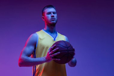 Stüdyoda kaslı bir adamın fotoğrafı, topuyla ayakta duran basketbolcu mor arka planda neon ışıkta izole edilmiş. Hedefler, spor, hareket, aktivite kavramları.