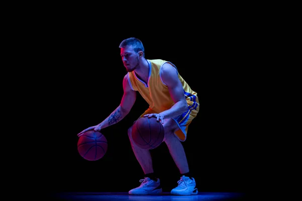 Goteando. Un hombre deportivo, jugador de baloncesto profesional jugando baloncesto aislado sobre fondo oscuro en luz de neón. Logros, carrera deportiva, conceptos de movimiento. —  Fotos de Stock