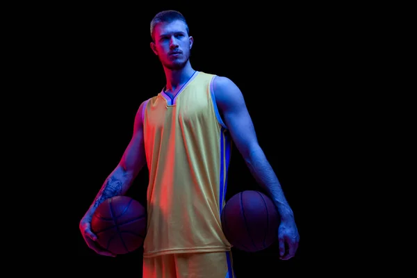 Portret van sportieve man, professionele basketbalspeler die geïsoleerd poseert op donkere achtergrond in neon licht. Resultaten, sportcarrière, bewegingsconcepten. — Stockfoto
