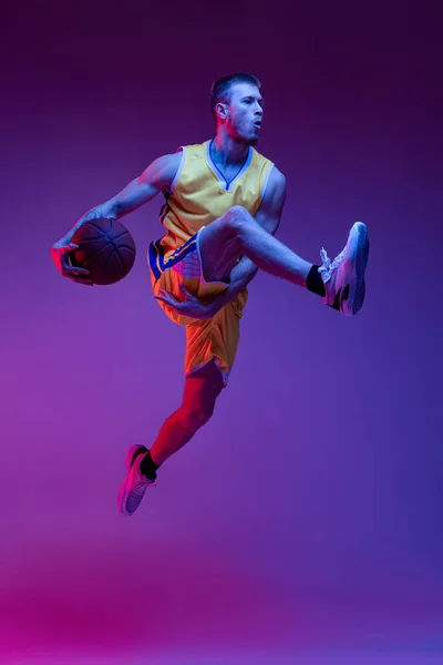 Studio shot van gespierde man, basketbal speler training met bal geïsoleerd op paarse achtergrond in neon licht. Doelstellingen, sport, beweging, activiteitsconcepten. — Stockfoto