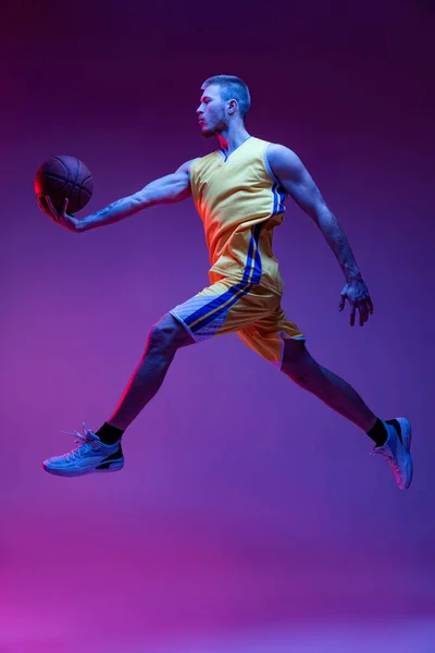 Studio shot of muscled man, basketball player training with ball isolated on purple background in neon light. Goals, sport, motion, activity concepts. — Stock Photo, Image