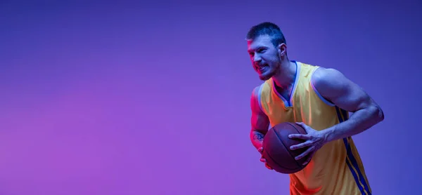 Studio záběr svalnatý muž, basketbalista trénink s míčem izolované na fialovém pozadí v neonovém světle. Cíle, sport, pohyb, koncepce aktivit. — Stock fotografie