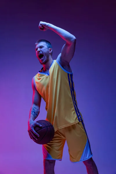 Un hombre emocionado, jugador de baloncesto gritando aislado sobre fondo púrpura en luz de neón. Objetivos, deporte, movimiento, conceptos de actividad. — Foto de Stock
