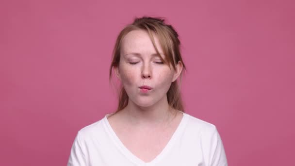 若い美しい女の子は、ピンクの背景に孤立した魚の顔を作る、そばかすのグリームを持つ。4K 、ビデオ。感情、表情の概念 — ストック動画
