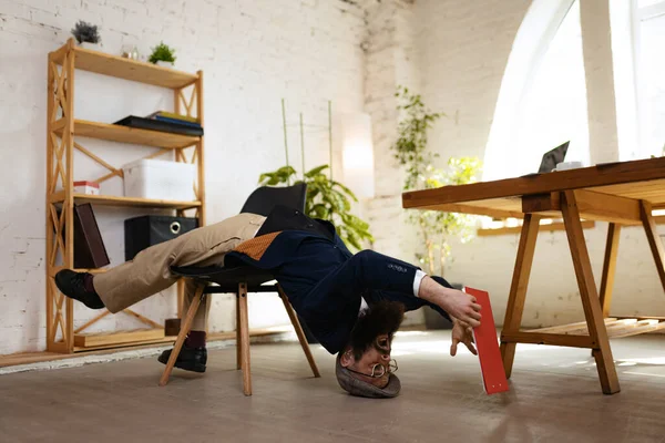 Un hombre, empleado de oficina que usa ropa de estilo empresarial que se divierte, haciendo yoga en la mesa de madera en la oficina moderna a la hora del trabajo con gadgets. Concepto de deporte, hobby — Foto de Stock