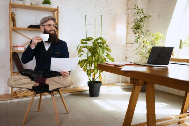 Genç sakallı bir adam, ofis çalışanı, modern ofiste aletlerle ahşap masada yoga yapıyor. İş anlayışı, sağlıklı yaşam tarzı, spor, hobi