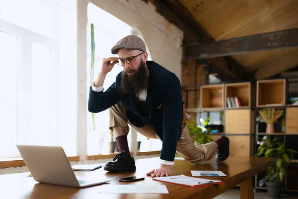 Joven barbudo, empleado de oficina divirtiéndose, haciendo yoga sobre mesa de madera en oficina moderna a la hora del trabajo con gadgets. Concepto de negocio, estilo de vida saludable, deporte, hobby — Foto de Stock