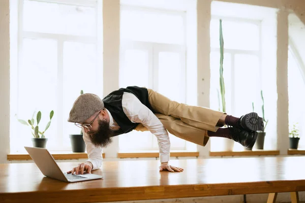 Empleado de oficina emocional, joven haciendo yoga en la mesa de madera en la oficina moderna en el tiempo de trabajo con gadgets. Concepto de negocio, estilo de vida saludable, deporte, hobby — Foto de Stock