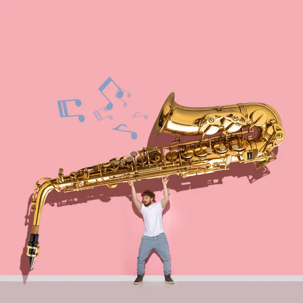 Creative design. Young man holding giant golden trumpet isolated over pink background — Stock Photo, Image
