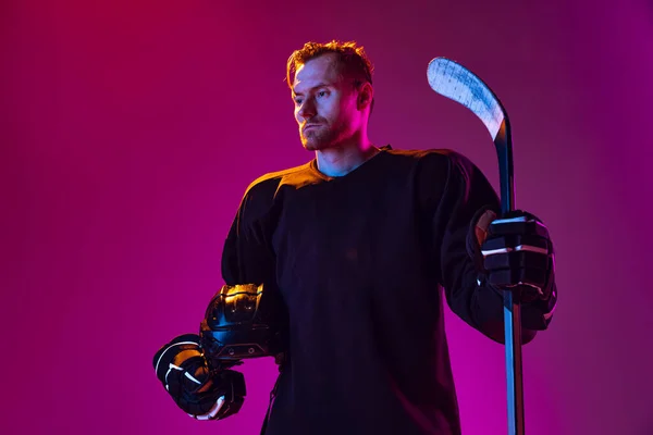 Potrait of concentrated man, professional hockey player in unifrom posting with stick isolated over pink background in neon light — Stok Foto