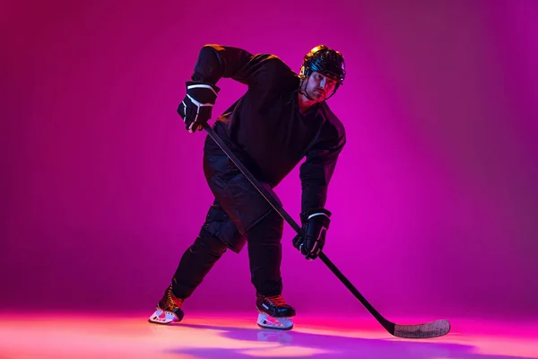 Portrait of active man, professional hockey player in motion, training isolated over pink background in neon light. Puck carrier